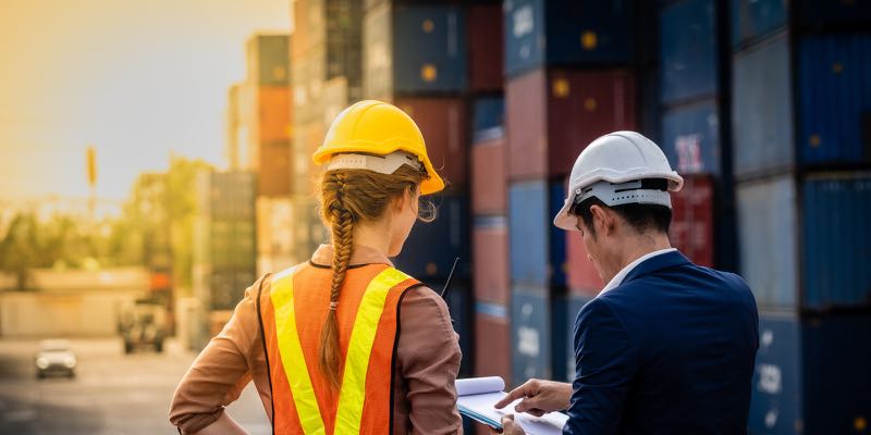 Two people in hard hats reviewing paperwork at a shipping yard